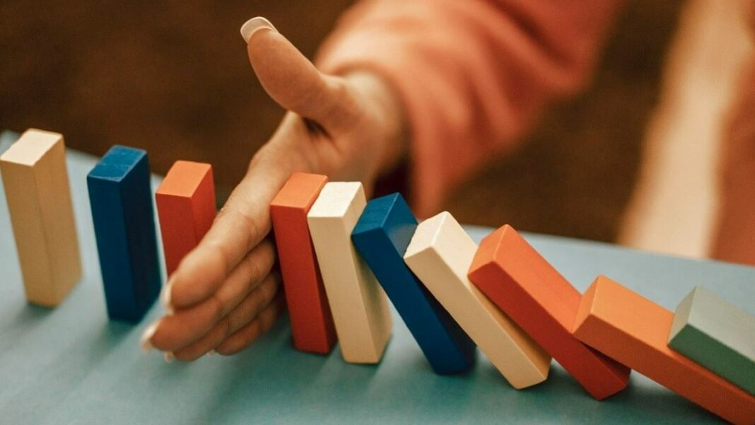 business risks represented by a woman's hand preventing a series of colored blocks from falling