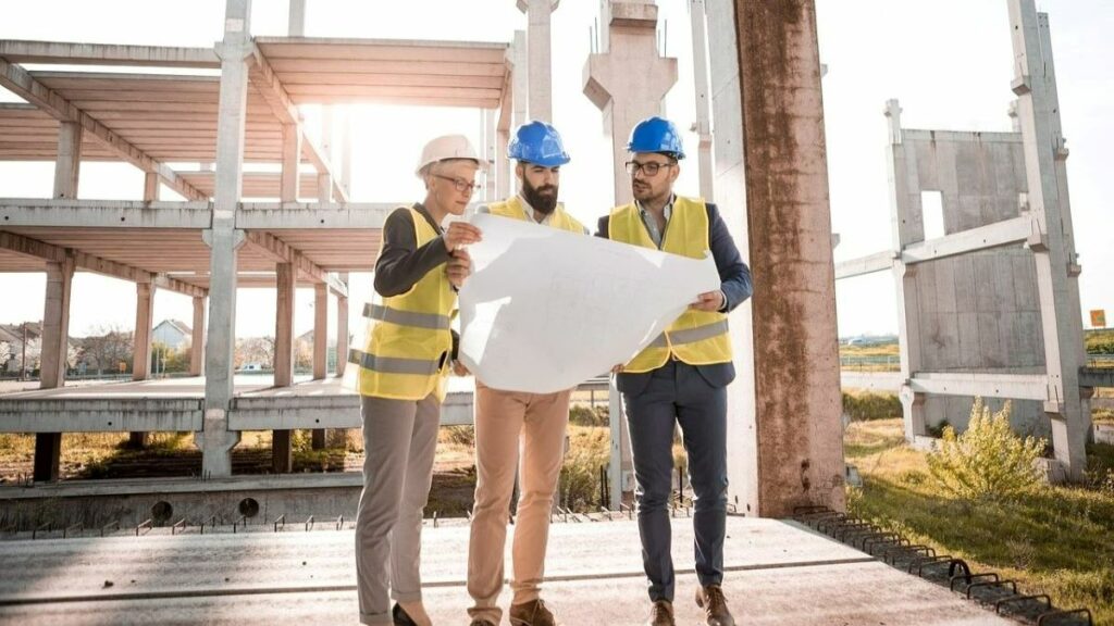 a career in construction represented by three people standing together on the flooring of a building under construction reviewing blueprints