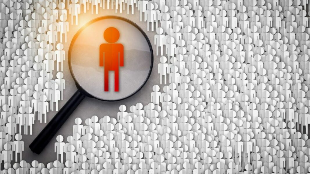 finding people on social media represented by a magnifying glass over a crowded field of paper cutouts