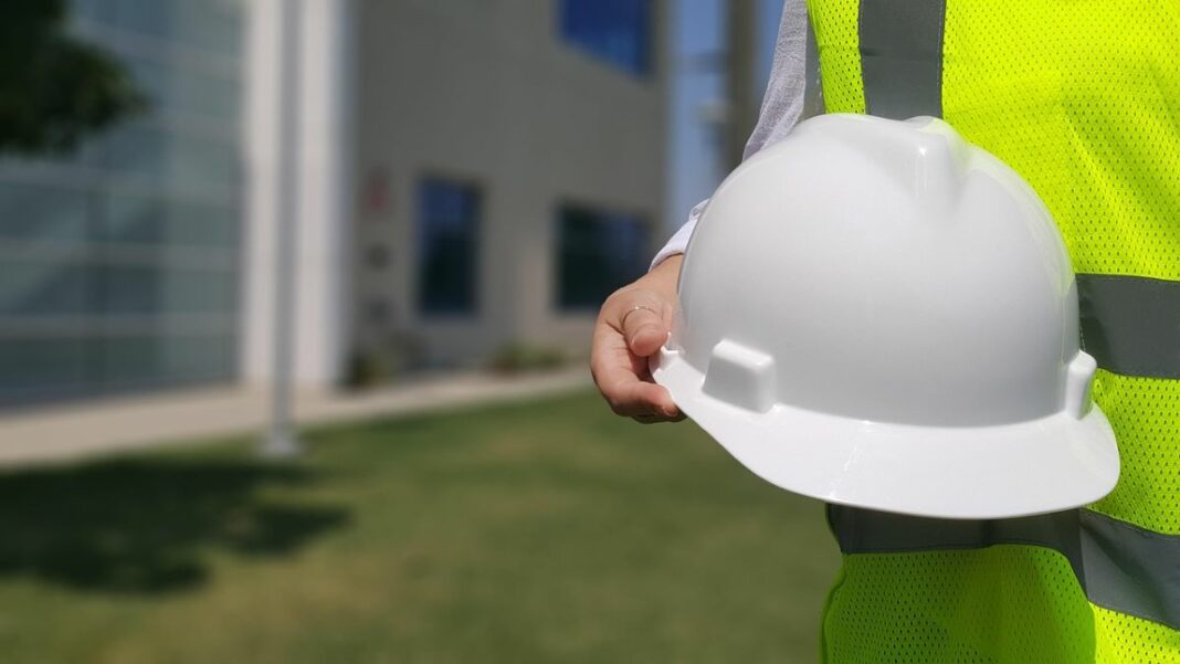 8 Ways to Simplify Your Next Construction Project - represented by a person wearing a neon green safety vest and holding a white hard hat
