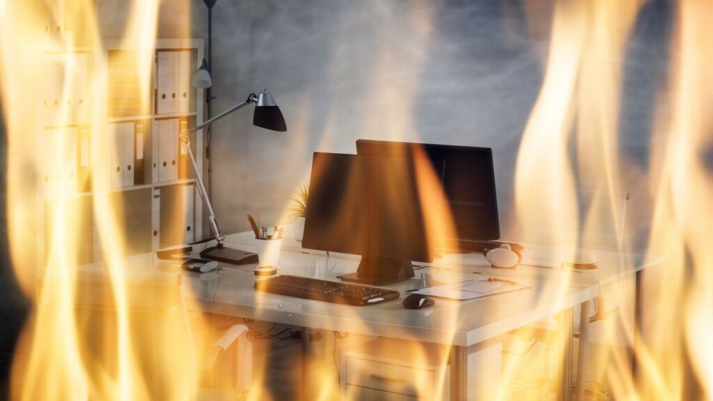 fire watch guard represented by flames in front of an office desk with an open laptop