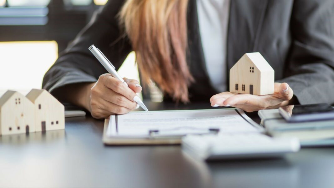 Streamline Your Rental Business - represented by a woman holding a wooden cutout of a house in one hand while making notes on a clipboard with the other hand