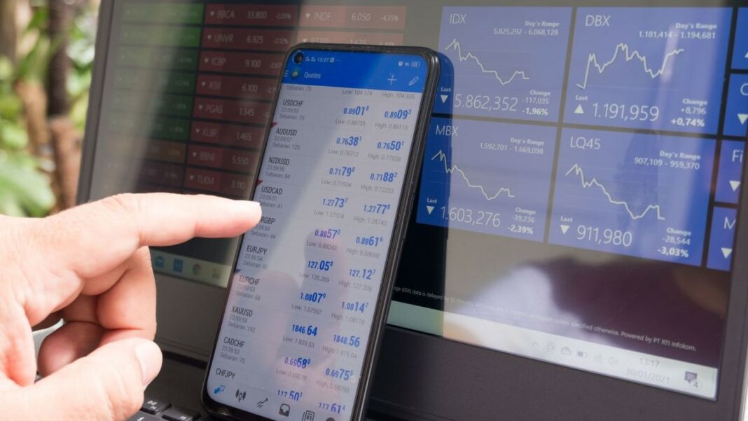 trading psychology represented by a hand pointing to a tablet next to a PC, both showing trading charts and graphs