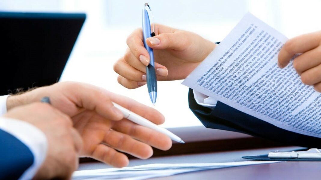breach of contract represented by a woman's hands and a man's hands, both holding pens and hovering over pages filled with fine print