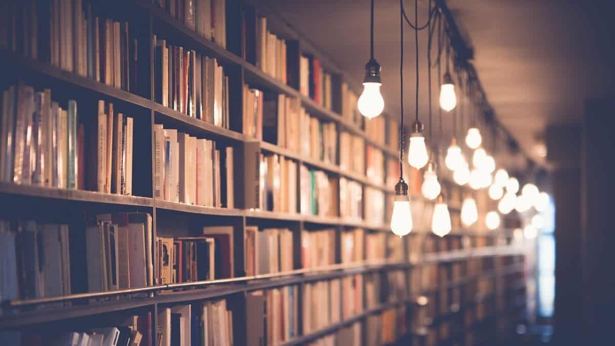 crypto books represented by a photo of stacks in an old library lit by a string of bare electric light bulbs