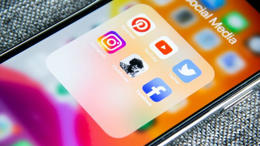 social media represented by a cell phone screen showing social media icons on a pink and orange background