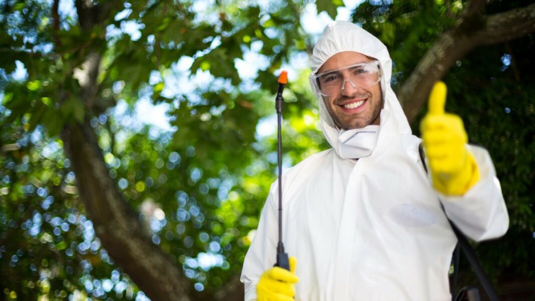 pest control represented by a portrait of a smiling man showing thumbs up while holding insecticide sprayer outdoors