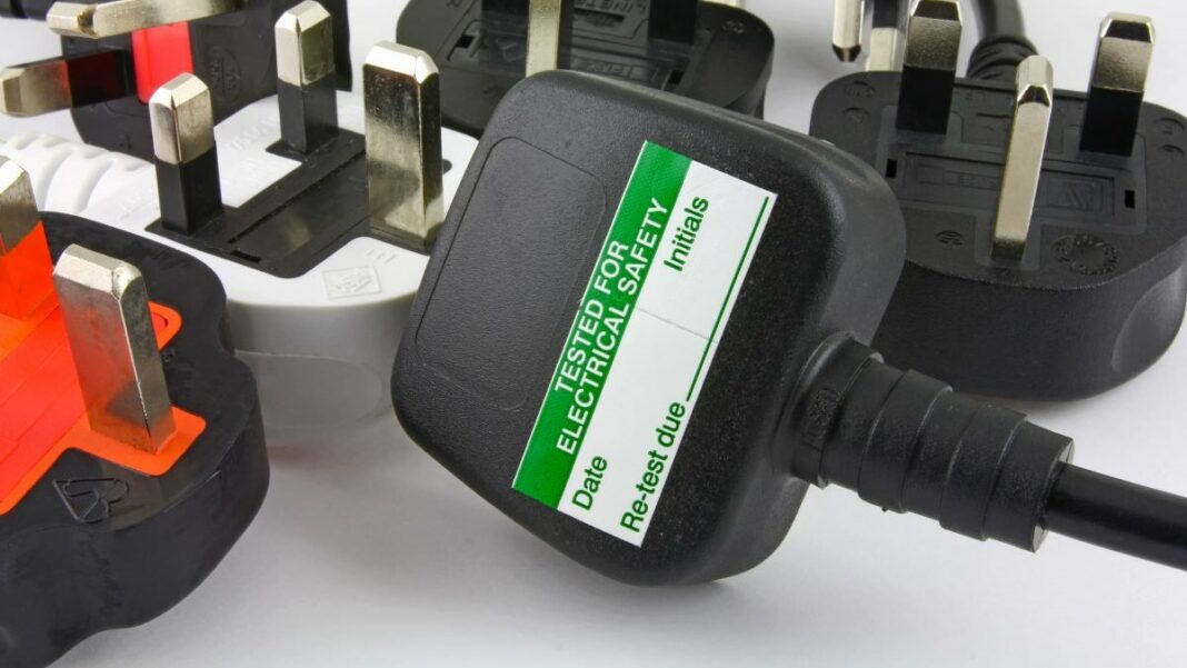 PAT testing represented by a side view of three-pin plugs showing the top of one plug with PAT test sticker