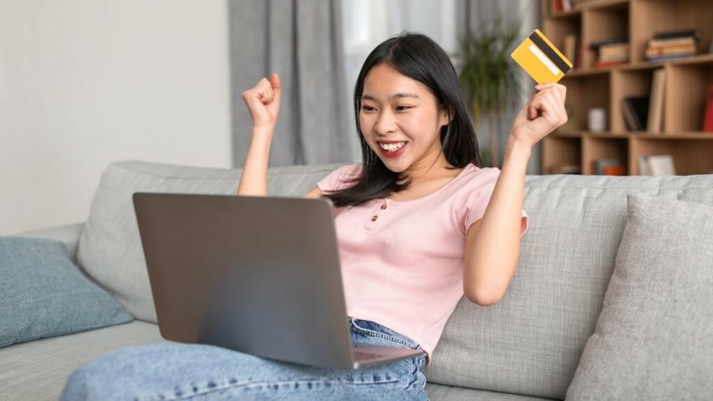 Japanese online casinos represented by a young woman sitting on a couch with an open laptop apparently happy about winning a game online