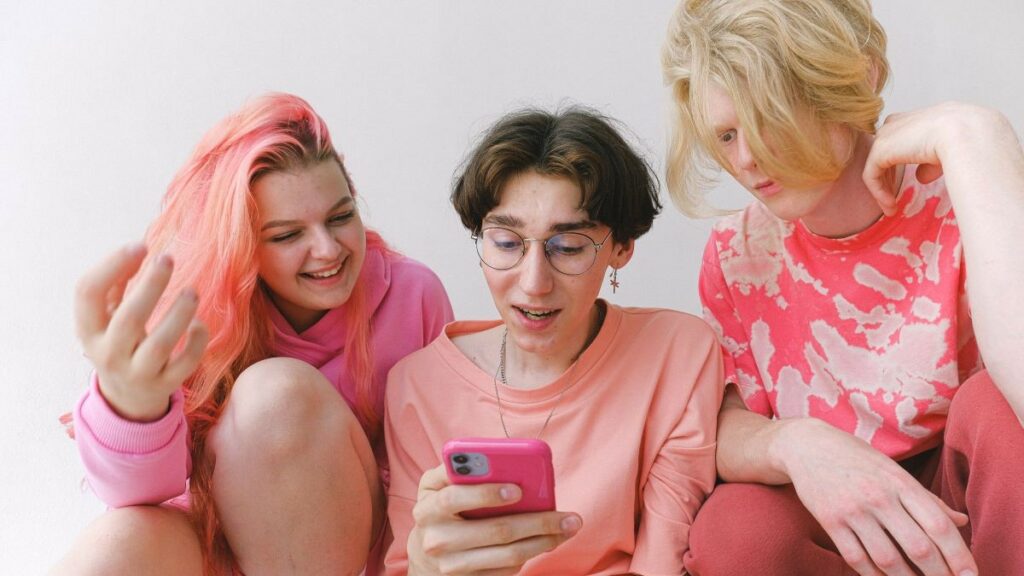 online entertainment represented by three teens having fun watching a video on a cell phone