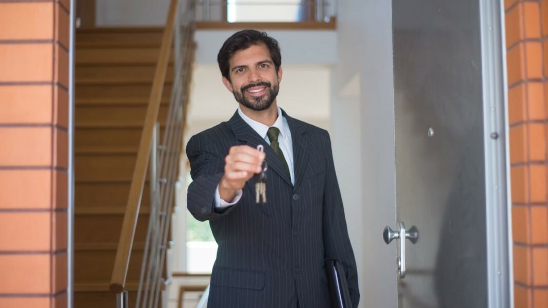 real estate investor represented by a man in a black suit holding out some keys at an open front door