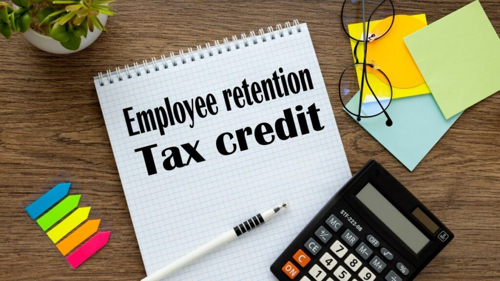 ERC tax credit represented by an overhead shot of a notepad with the words "Employee retention Tax credit" written on it, next to a calculator and some colorful sticky notes