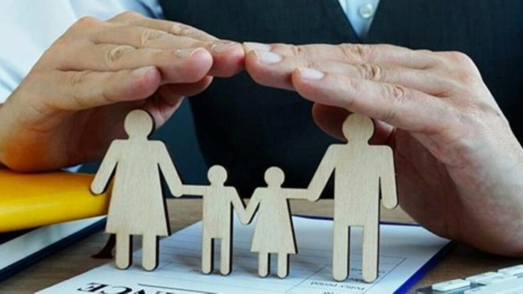 life insurance coverage represented by a man's hands protecting wooden cutouts of a family of four