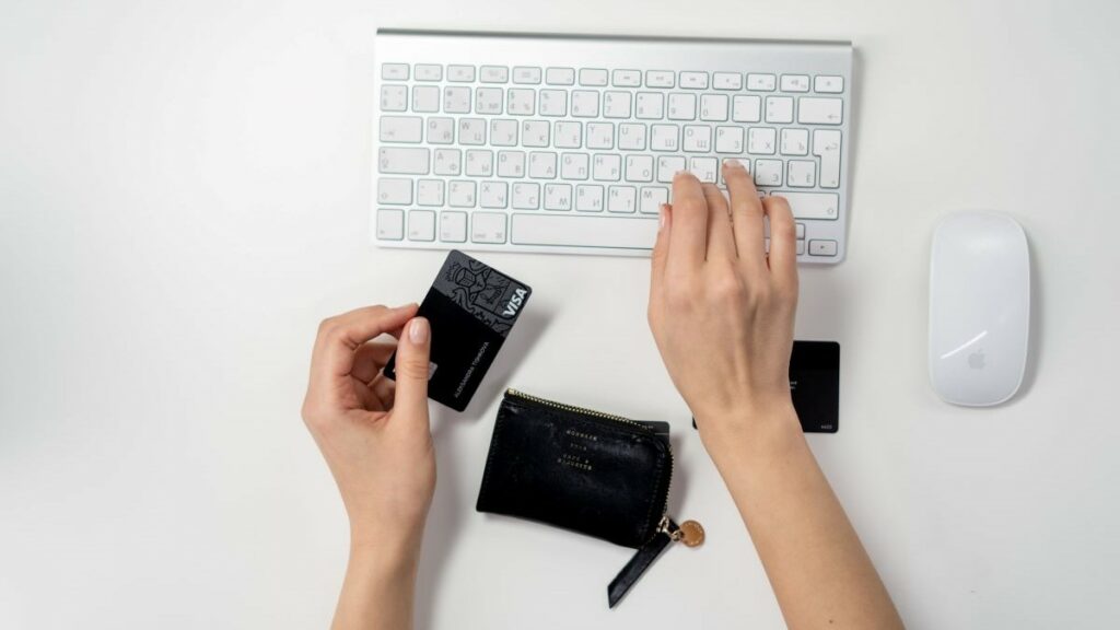 eCommerce business models represented by a woman's hands on a white background, as her right hand hovers over a white keyboard and her left hand holds a black credit card