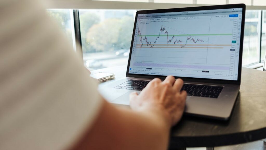 stock price fluctuations represented by a man poised in front of a laptop showing a stock market chart on the screen
