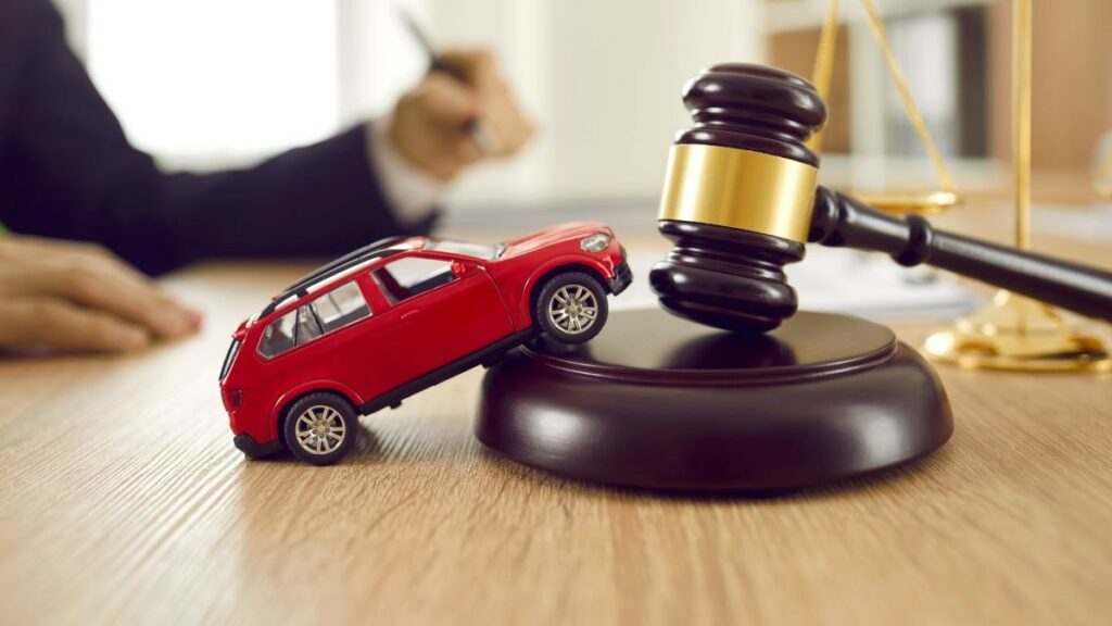 car accident and attorney represented by little red toy automobile on a wooden table with sound block and gavel